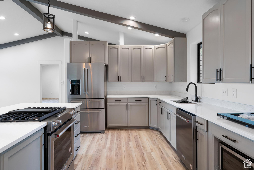 Kitchen featuring light hardwood / wood-style floors, lofted ceiling with beams, appliances with stainless steel finishes, gray cabinets, and sink