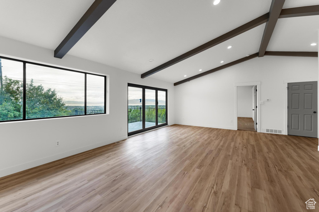 Empty room with vaulted ceiling with beams and light hardwood / wood-style flooring