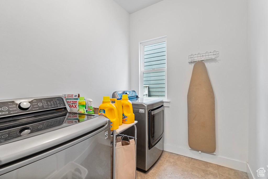 Clothes washing area with washer and dryer, a healthy amount of sunlight, and light tile floors