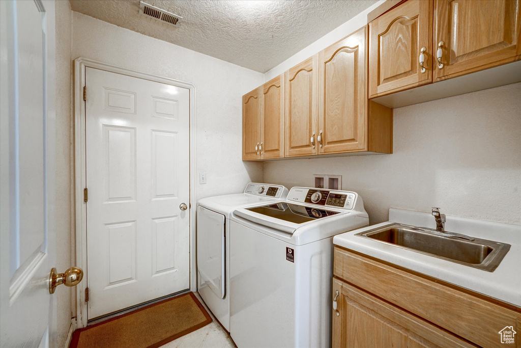 Laundry area featuring cabinets, a textured ceiling, washing machine and clothes dryer, sink, and light tile flooring