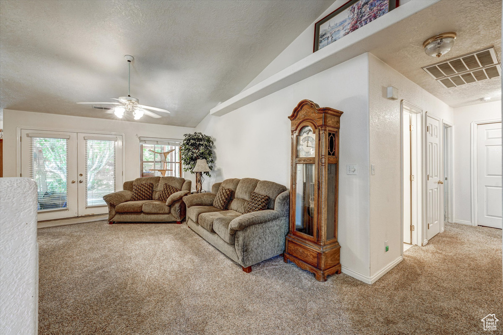 Carpeted living room with ceiling fan, vaulted ceiling, a textured ceiling, and french doors