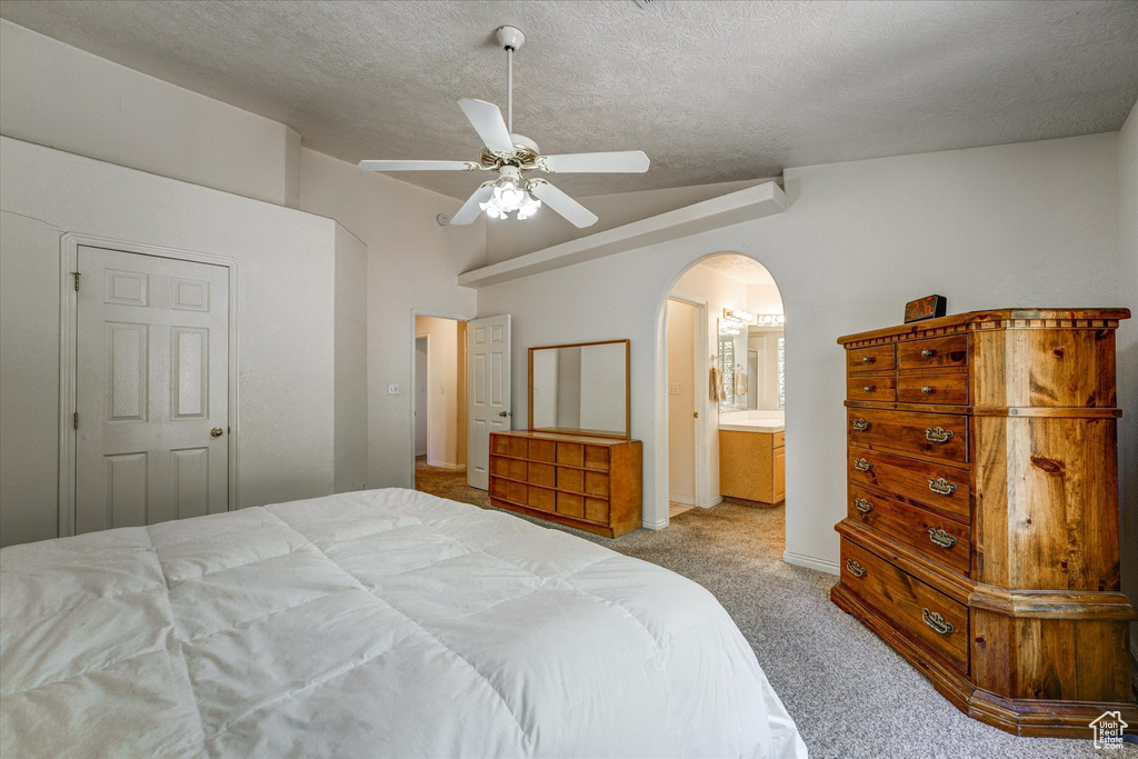 Carpeted bedroom featuring ceiling fan, a textured ceiling, lofted ceiling, and ensuite bathroom