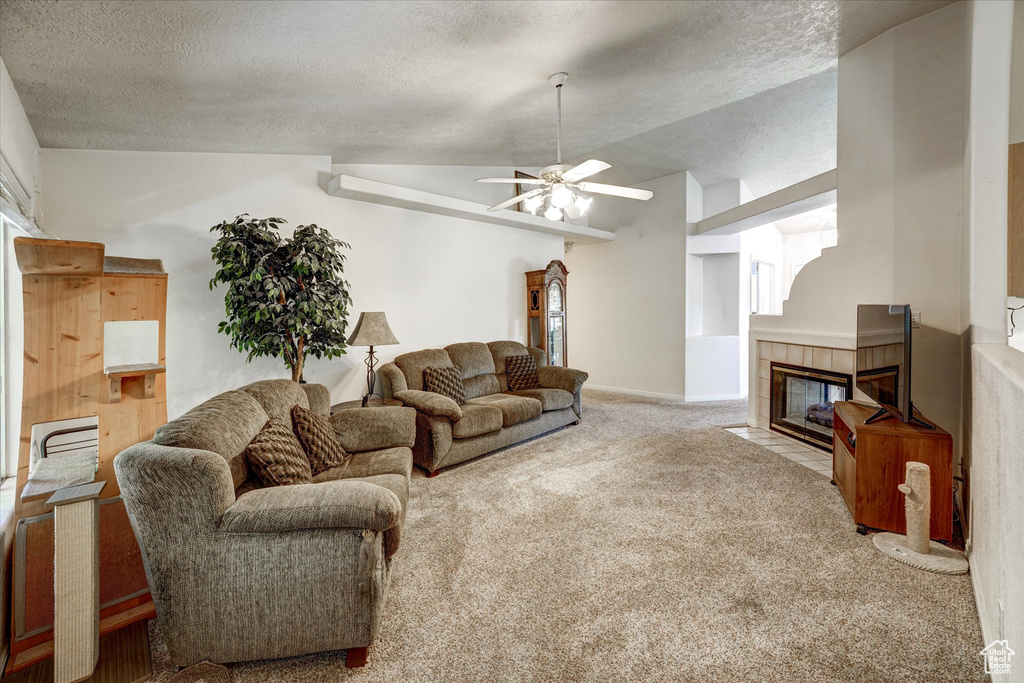 Carpeted living room featuring a textured ceiling, ceiling fan, a fireplace, and lofted ceiling