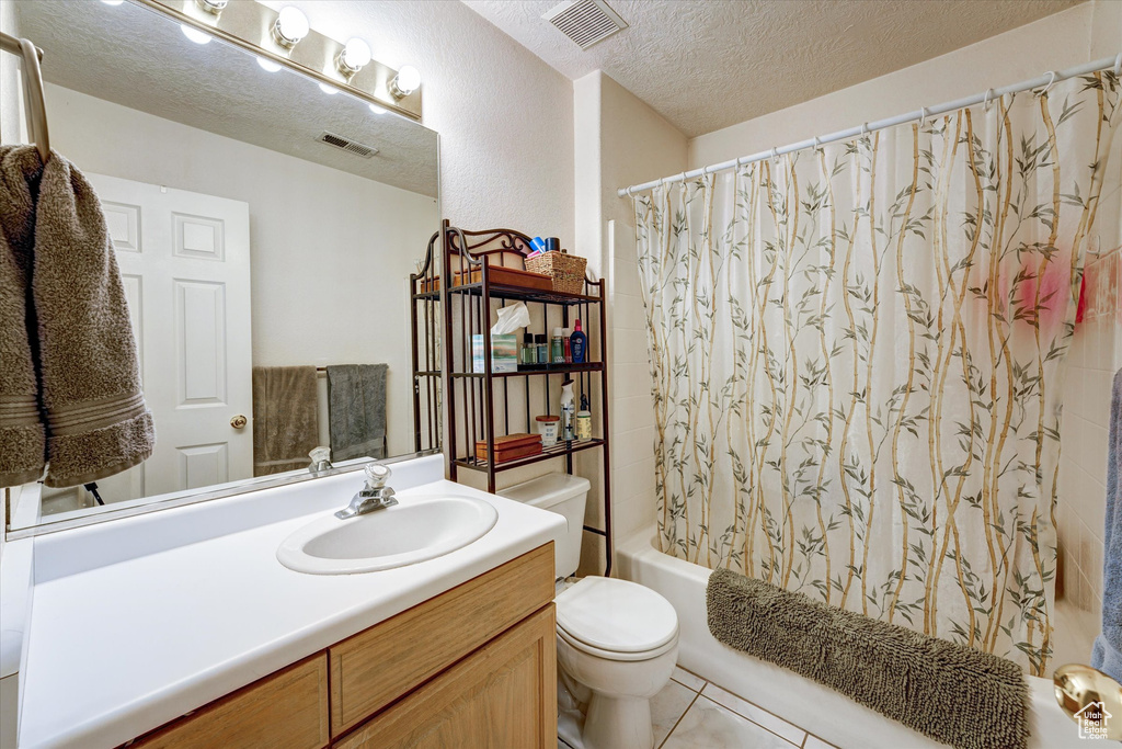Full bathroom with oversized vanity, toilet, tile floors, shower / bath combo with shower curtain, and a textured ceiling