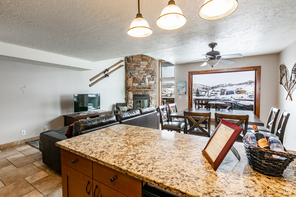 Kitchen featuring a stone fireplace, a textured ceiling, ceiling fan, and light tile floors