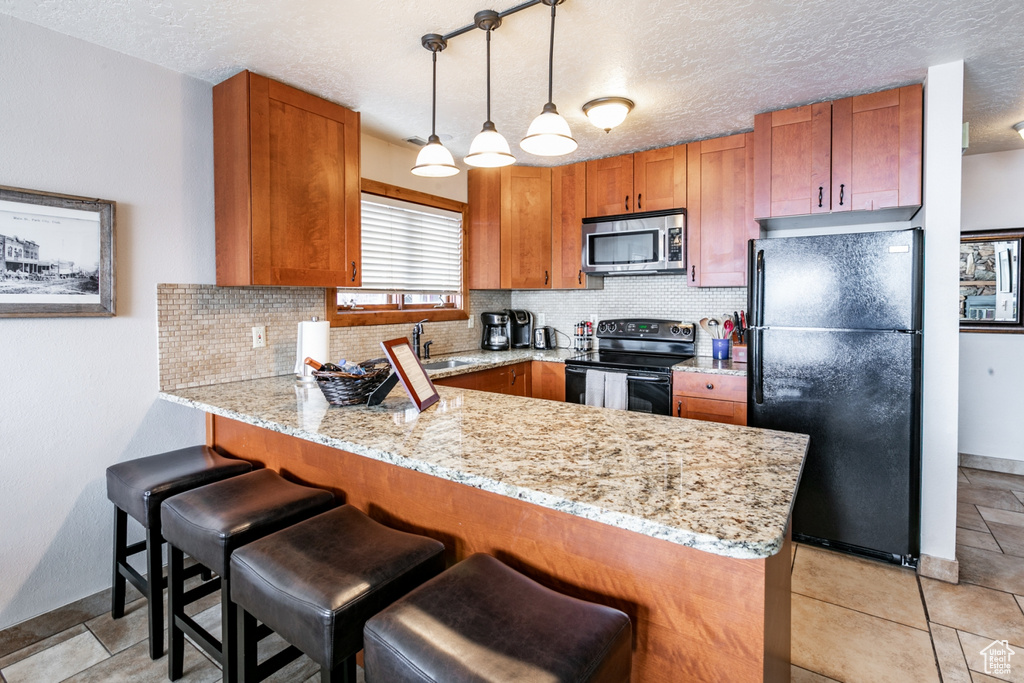 Kitchen featuring kitchen peninsula, light tile flooring, black appliances, backsplash, and hanging light fixtures