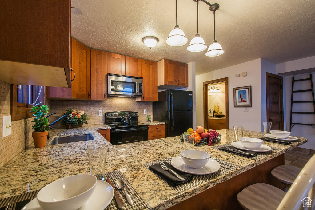 Kitchen featuring tasteful backsplash, decorative light fixtures, black appliances, a textured ceiling, and sink