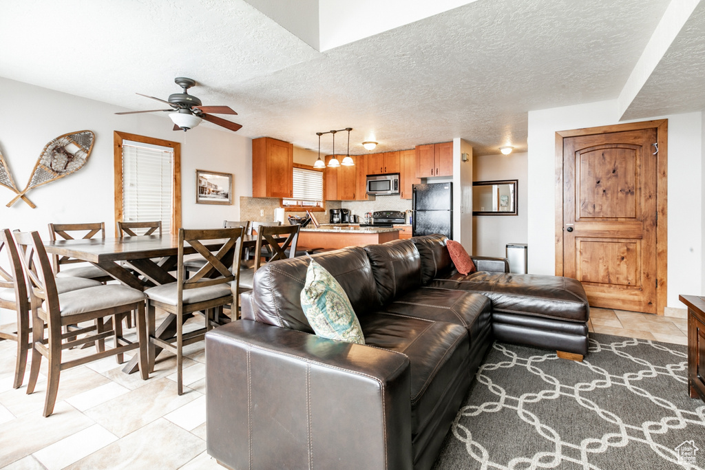 Living room featuring ceiling fan, a textured ceiling, and light tile flooring