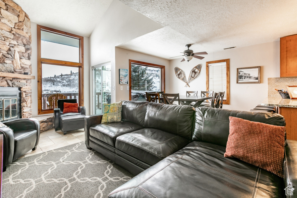 Living room with a fireplace, ceiling fan, a textured ceiling, and light tile floors