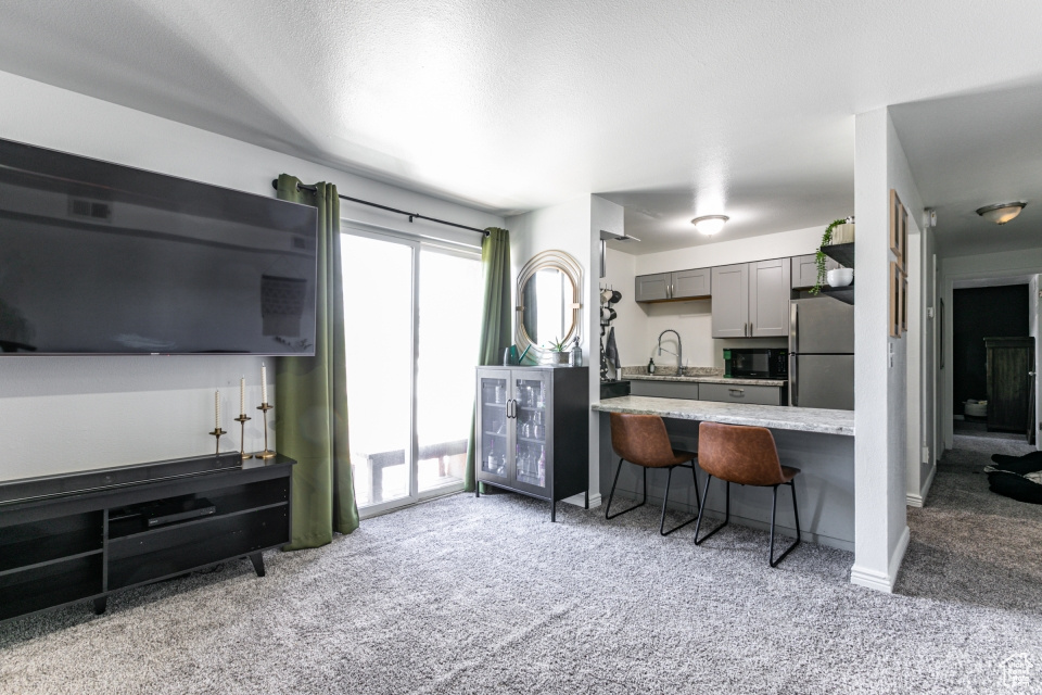 Kitchen featuring stainless steel refrigerator, carpet, gray cabinets, sink, and a breakfast bar