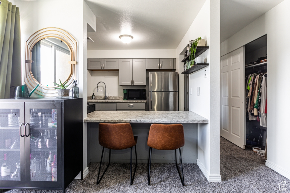 Kitchen featuring dark carpet, gray cabinets, sink, a breakfast bar, and stainless steel refrigerator