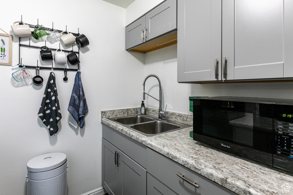 Kitchen featuring gray cabinetry, light stone countertops, and sink