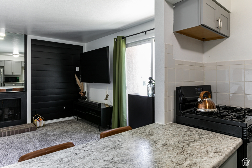 Kitchen with carpet, range with gas stovetop, a fireplace, backsplash, and gray cabinets