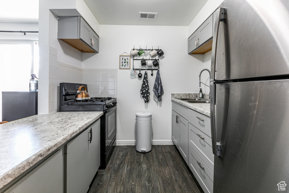 Kitchen featuring black range with gas stovetop, stainless steel refrigerator, dark hardwood / wood-style flooring, gray cabinets, and sink