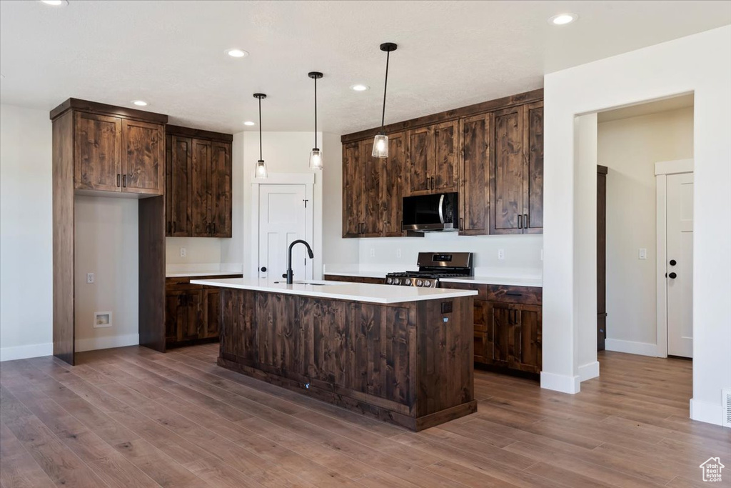 Kitchen with pendant lighting, hardwood / wood-style flooring, dark brown cabinetry, an island with sink, and stainless steel appliances