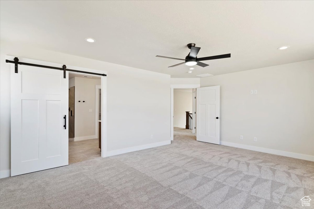 Unfurnished room with ceiling fan, a barn door, and light colored carpet