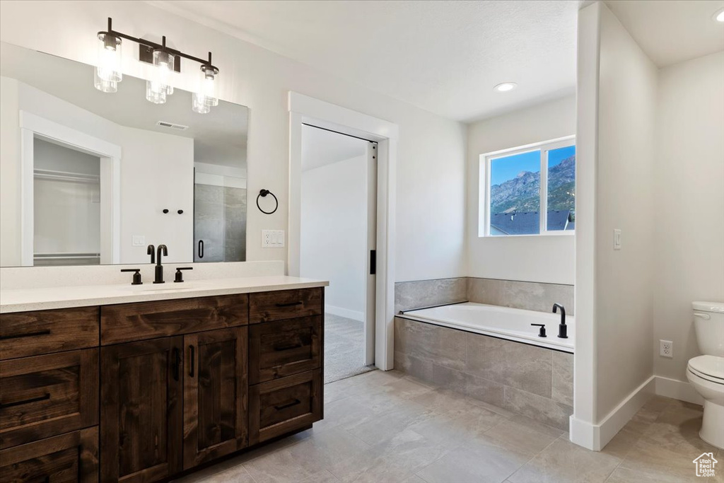 Bathroom featuring tile patterned floors, vanity, toilet, and tiled bath