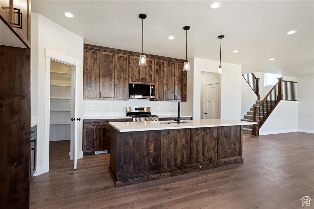 Kitchen featuring dark hardwood / wood-style floors, appliances with stainless steel finishes, dark brown cabinets, a center island with sink, and sink