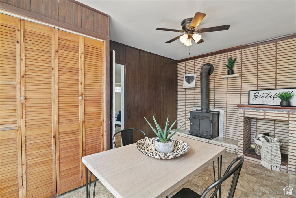 Dining room with wood walls, light tile flooring, ceiling fan, and a wood stove