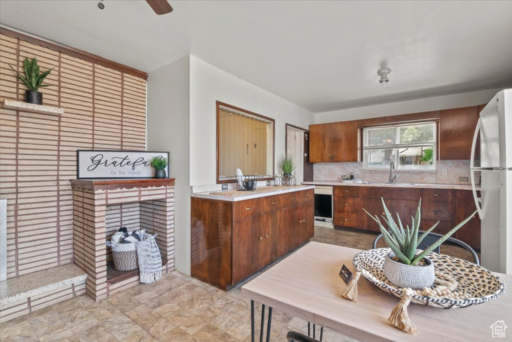 Kitchen featuring ceiling fan, white fridge, backsplash, light tile floors, and sink