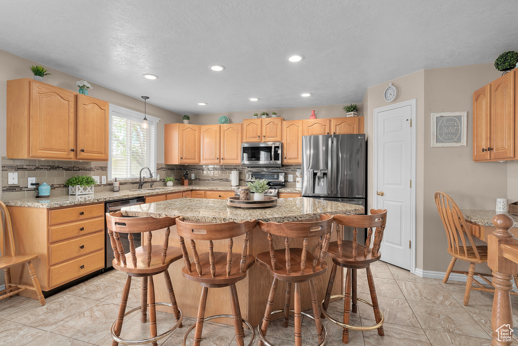 Kitchen with stainless steel appliances, a center island, tasteful backsplash, and light stone countertops