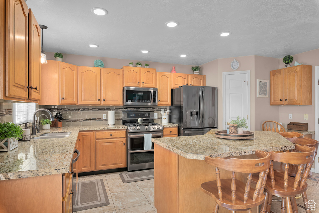 Kitchen with a kitchen breakfast bar, appliances with stainless steel finishes, light stone counters, tasteful backsplash, and light tile floors