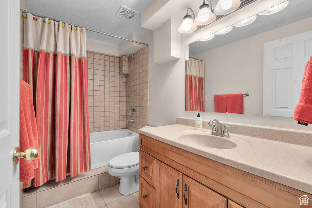 Full bathroom with toilet, tile floors, shower / bath combo with shower curtain, vanity, and a textured ceiling