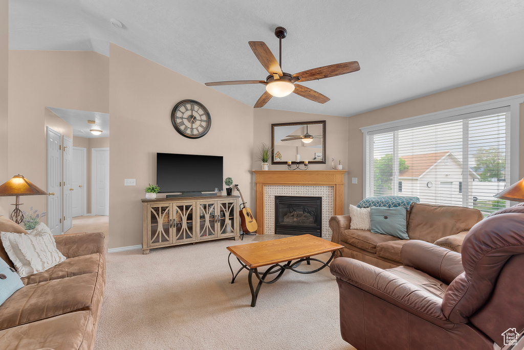 Living room featuring light carpet, a tiled fireplace, ceiling fan, and lofted ceiling