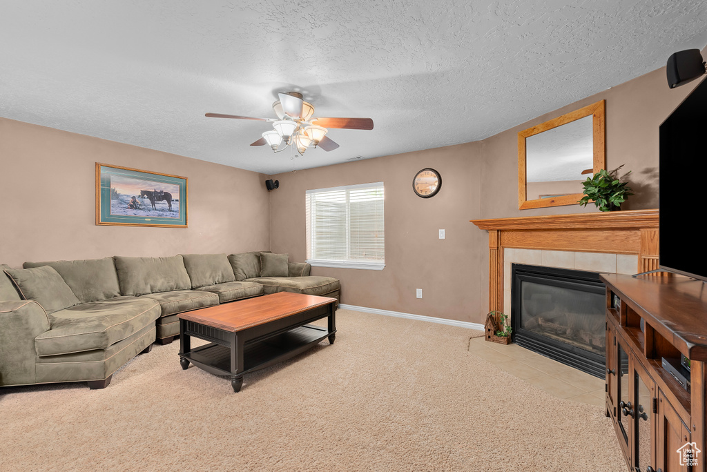 Living room featuring light carpet, ceiling fan, a tile fireplace, and a textured ceiling