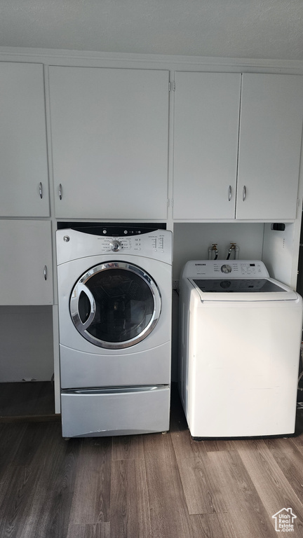 Laundry area featuring hookup for a washing machine, separate washer and dryer, hardwood / wood-style flooring, and cabinets