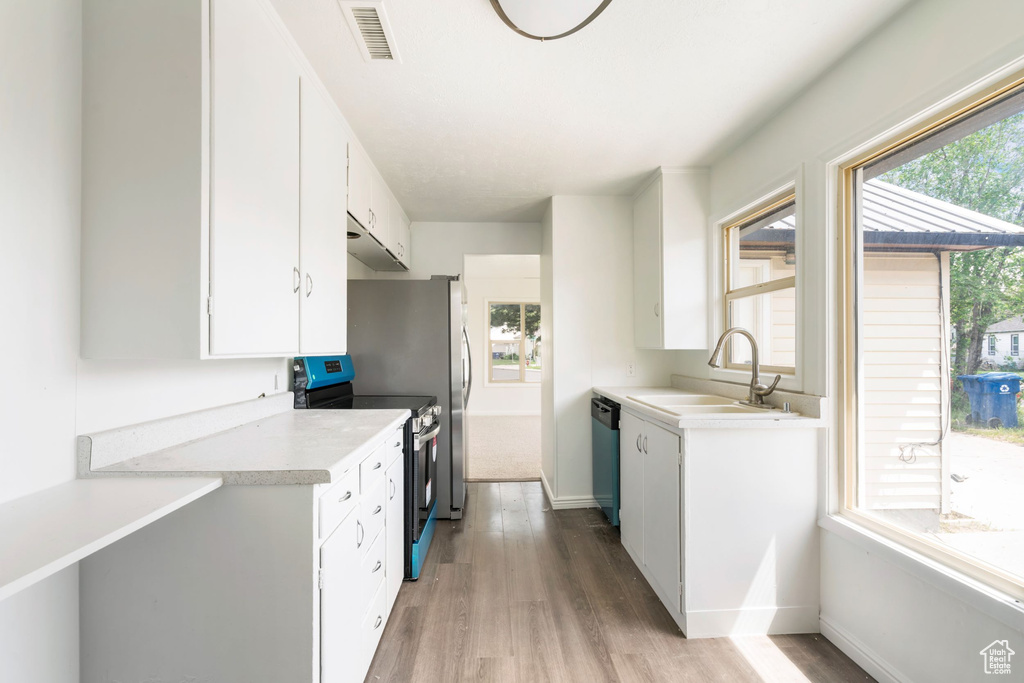 Kitchen with appliances with stainless steel finishes, white cabinetry, sink, and light hardwood / wood-style flooring