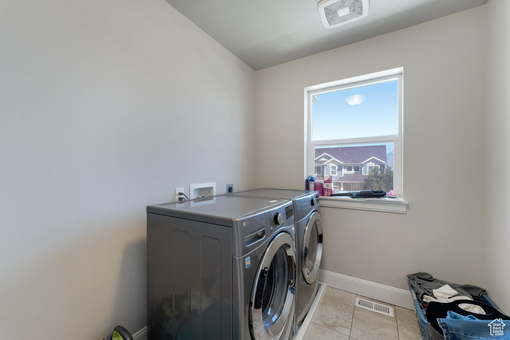 Laundry area with separate washer and dryer, hookup for an electric dryer, hookup for a washing machine, and light tile floors