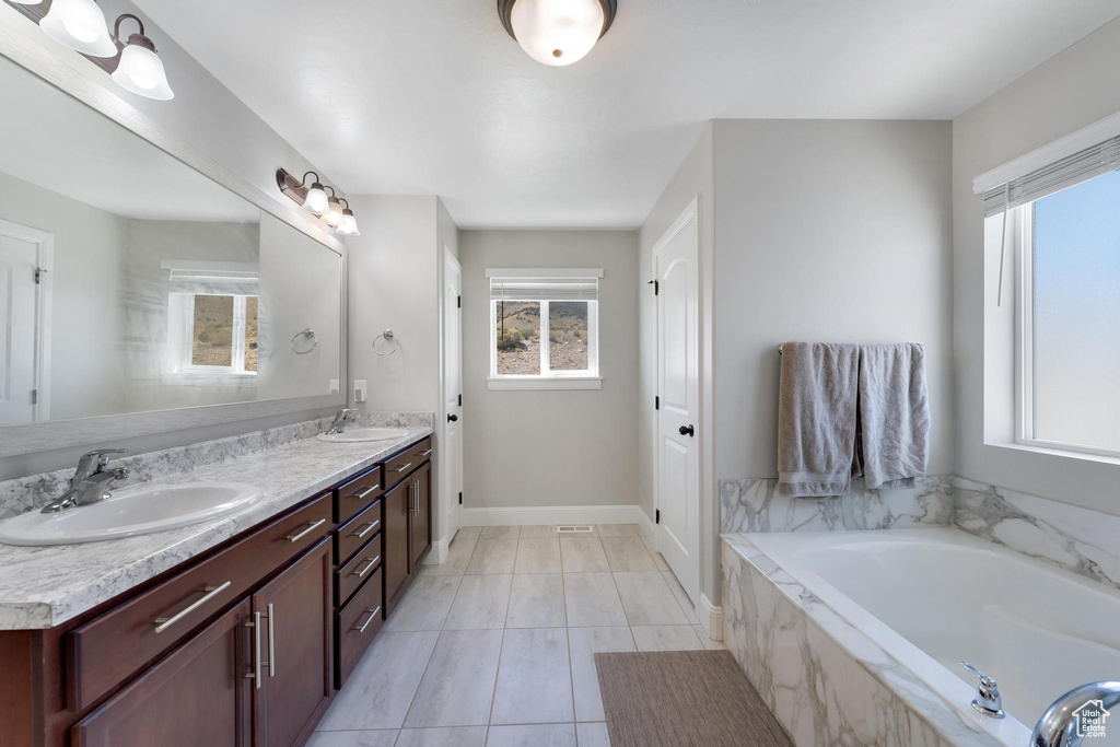 Bathroom featuring a wealth of natural light, tile flooring, double sink vanity, and a relaxing tiled bath