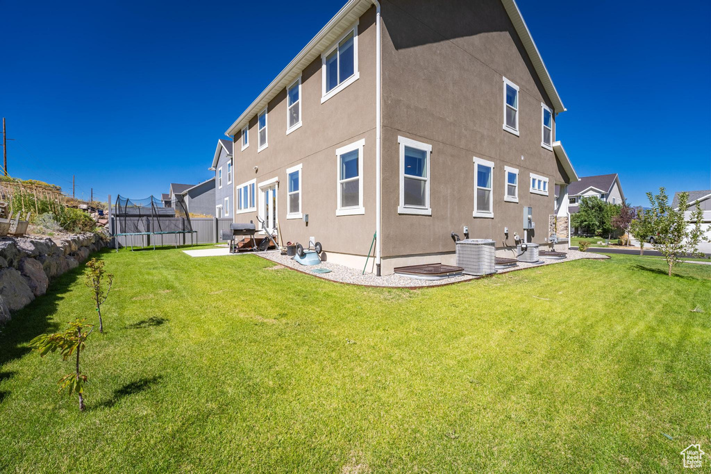 Back of property with a trampoline, a patio area, and a lawn