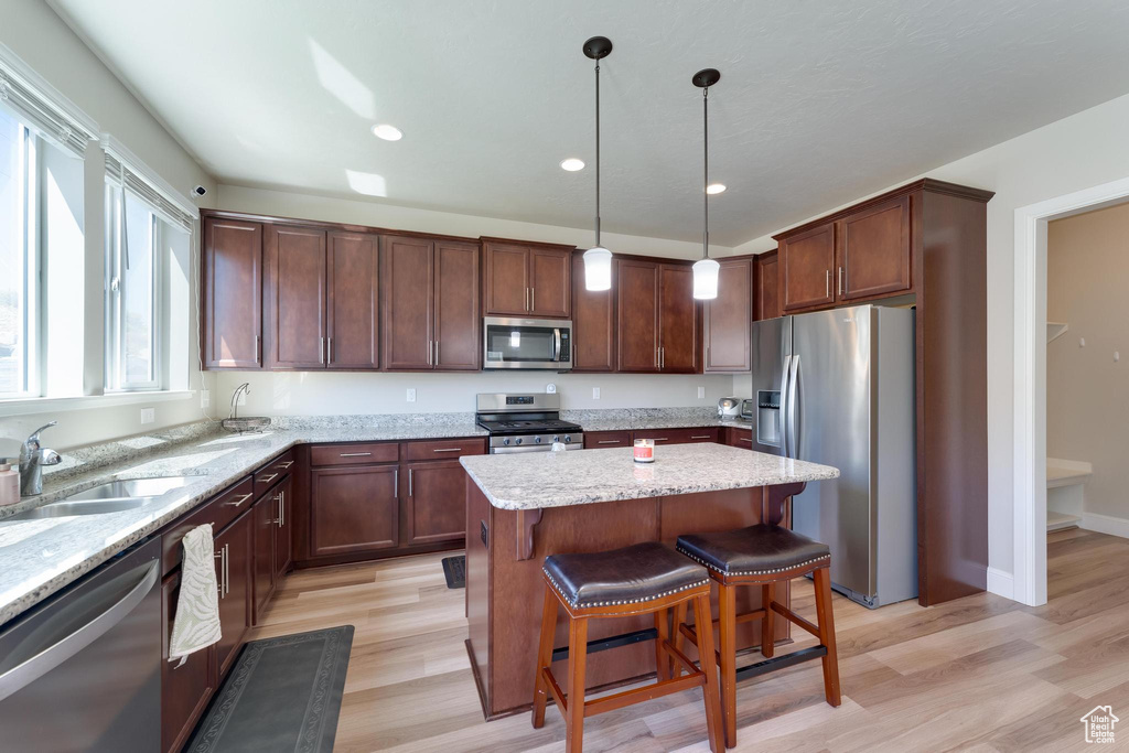 Kitchen with light stone counters, light hardwood / wood-style floors, hanging light fixtures, a center island, and appliances with stainless steel finishes