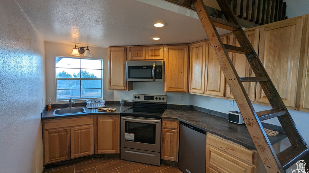 Kitchen featuring appliances with stainless steel finishes, sink, dark tile flooring, and a textured ceiling