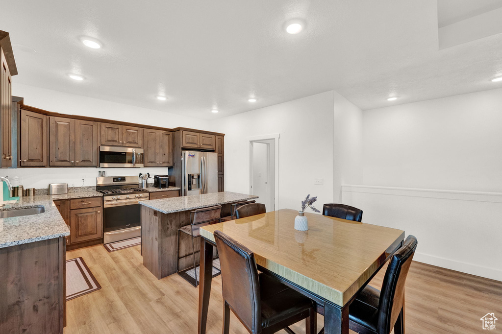 Kitchen with light stone counters, light hardwood / wood-style flooring, stainless steel appliances, a center island, and sink