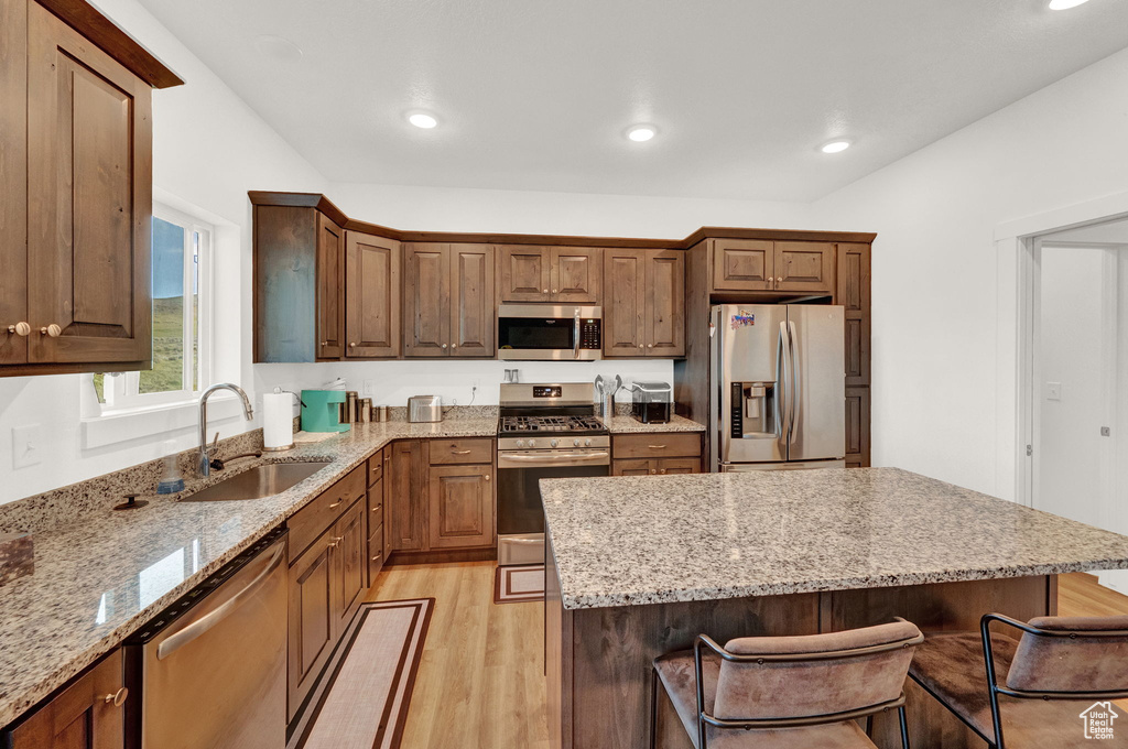 Kitchen featuring light stone countertops, light hardwood / wood-style flooring, a kitchen island, sink, and appliances with stainless steel finishes