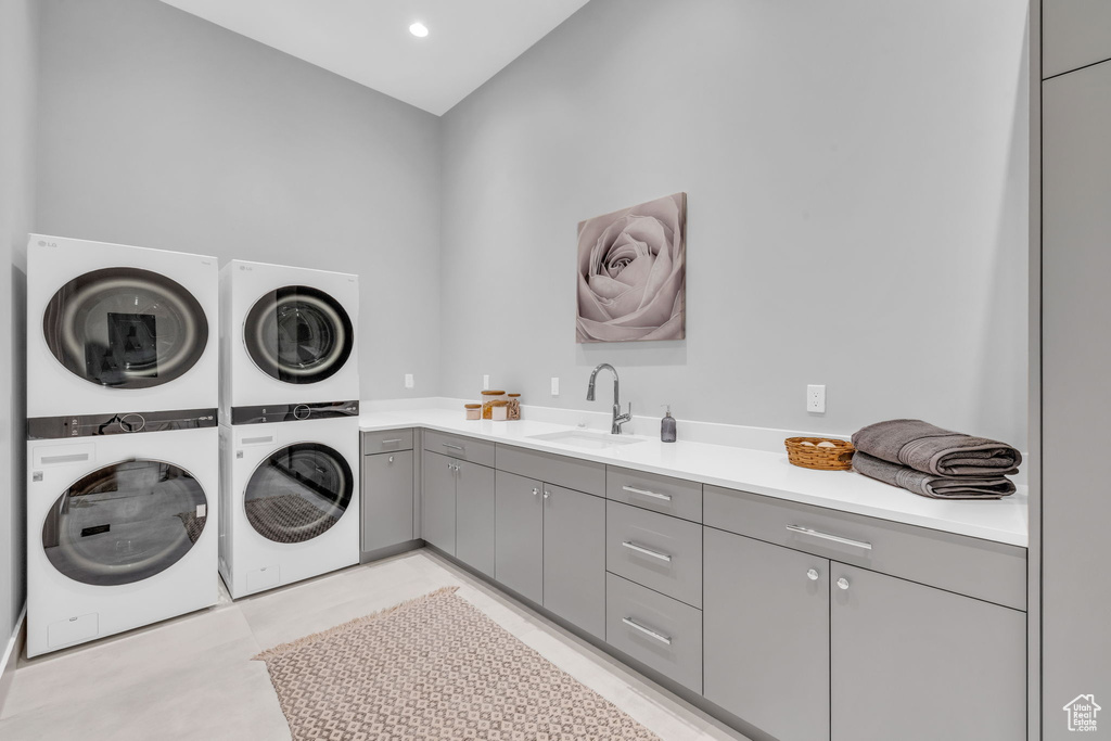 Laundry room with sink, stacked washer and clothes dryer, cabinets, and light tile patterned floors