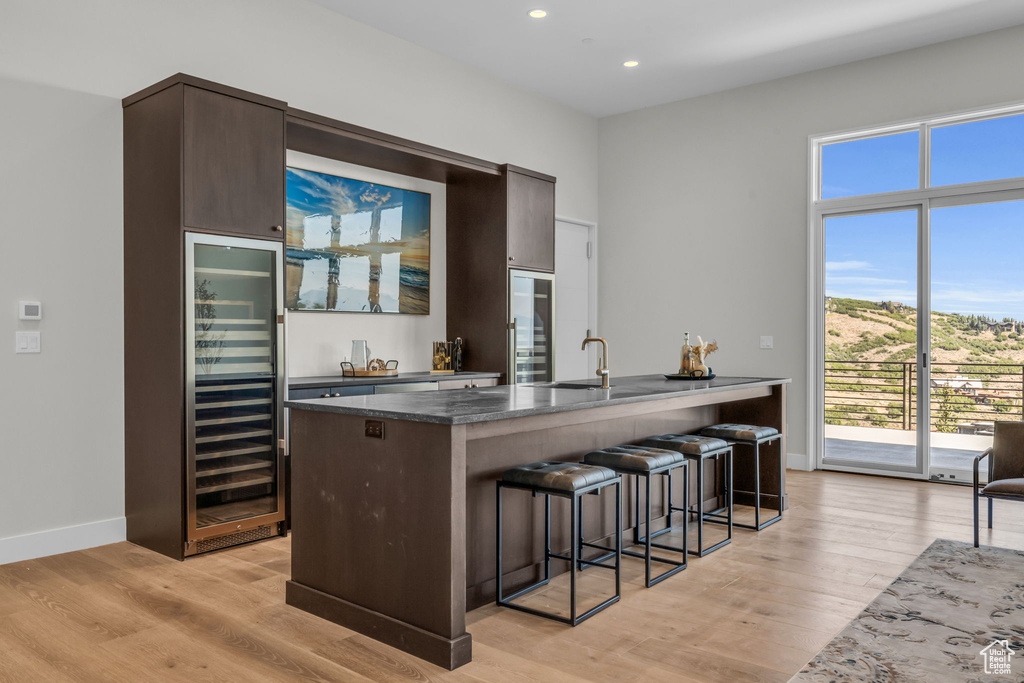 Kitchen with dark brown cabinets, light wood-type flooring, dark stone counters, a kitchen bar, and sink