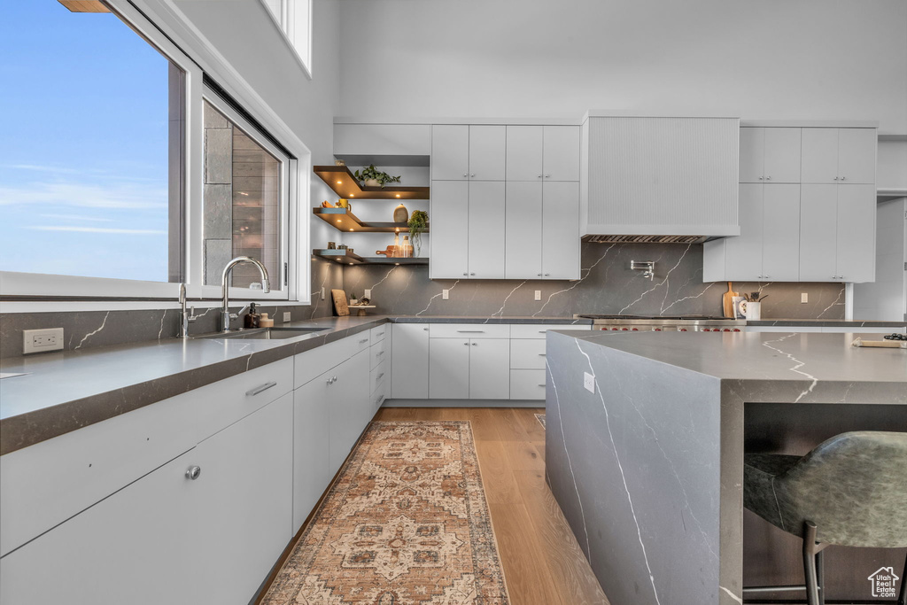 Kitchen with sink, backsplash, white cabinetry, and light wood-type flooring