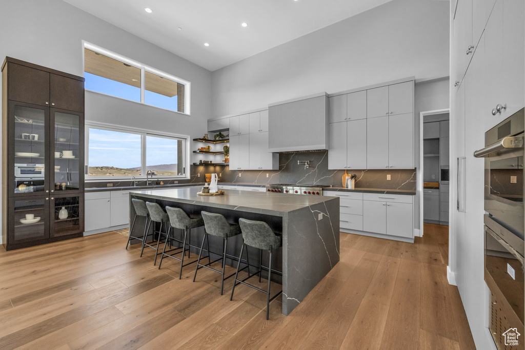 Kitchen featuring a kitchen bar, backsplash, a kitchen island, a high ceiling, and light wood-type flooring