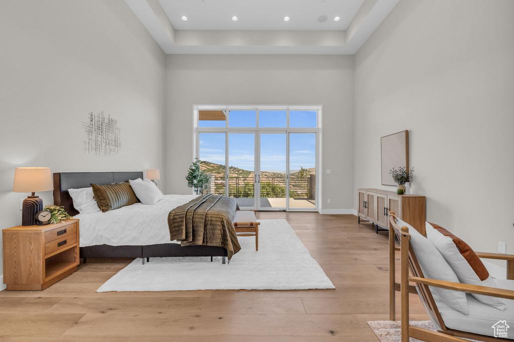 Bedroom featuring a high ceiling, access to outside, a raised ceiling, and light hardwood / wood-style floors