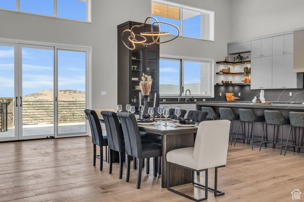 Dining room with a chandelier, light wood-type flooring, a wealth of natural light, and a high ceiling