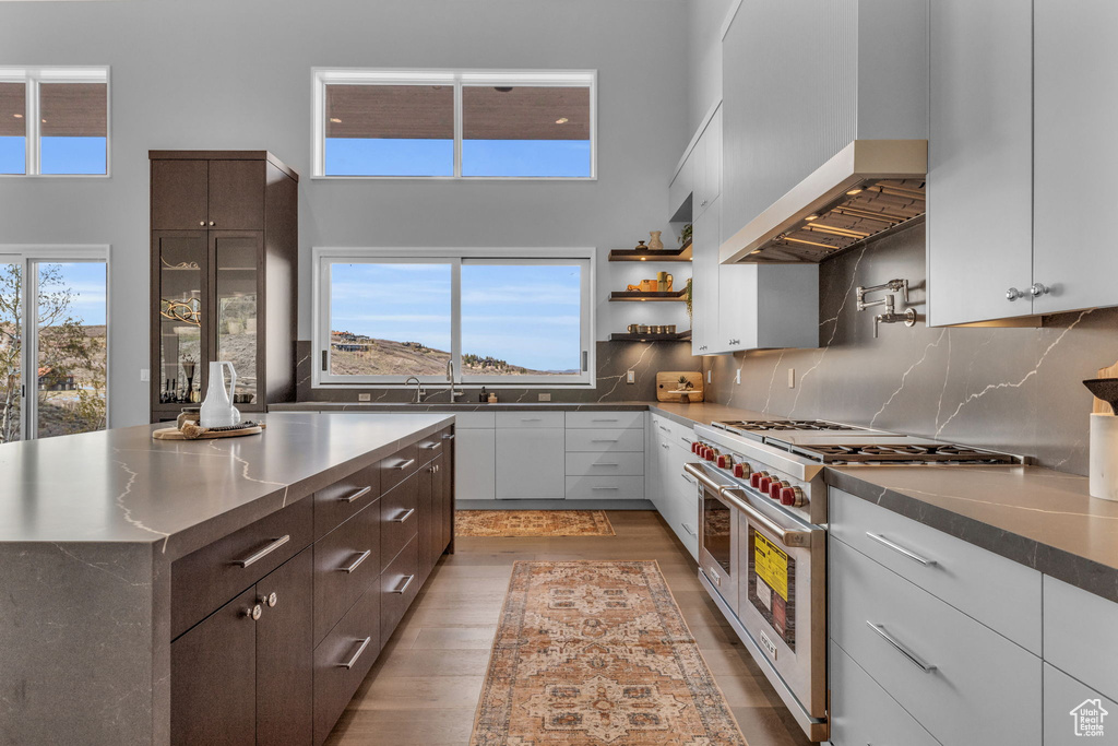 Kitchen with a high ceiling, decorative backsplash, hardwood / wood-style floors, wall chimney exhaust hood, and double oven range