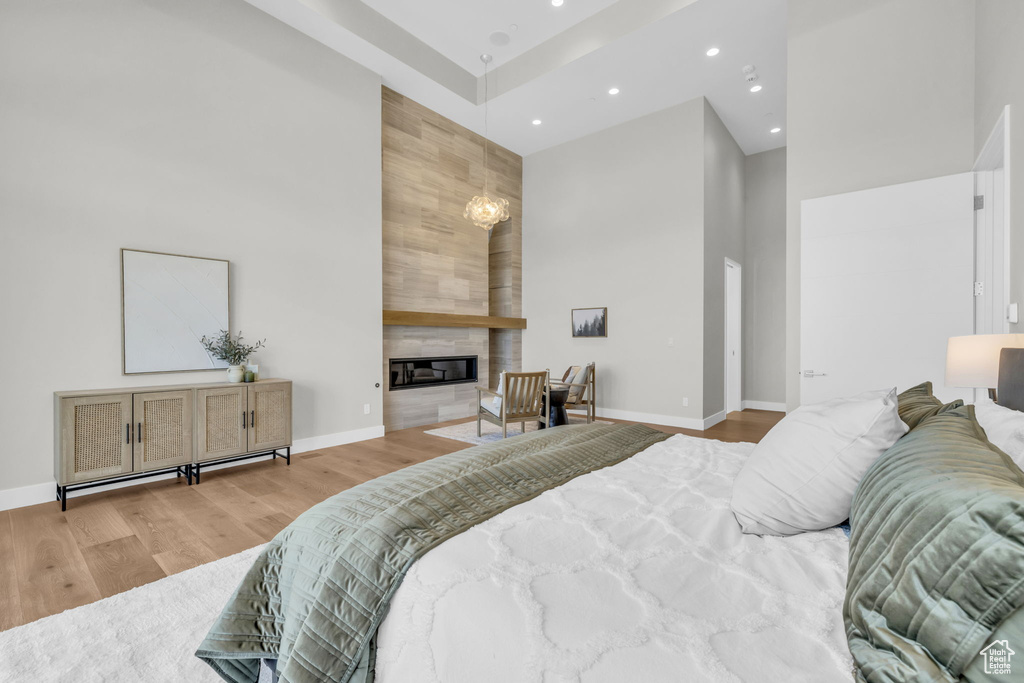 Bedroom featuring a towering ceiling, light wood-type flooring, and a large fireplace