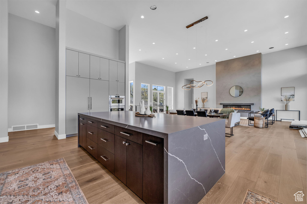 Kitchen with light hardwood / wood-style flooring, dark brown cabinets, a large island, a fireplace, and a towering ceiling