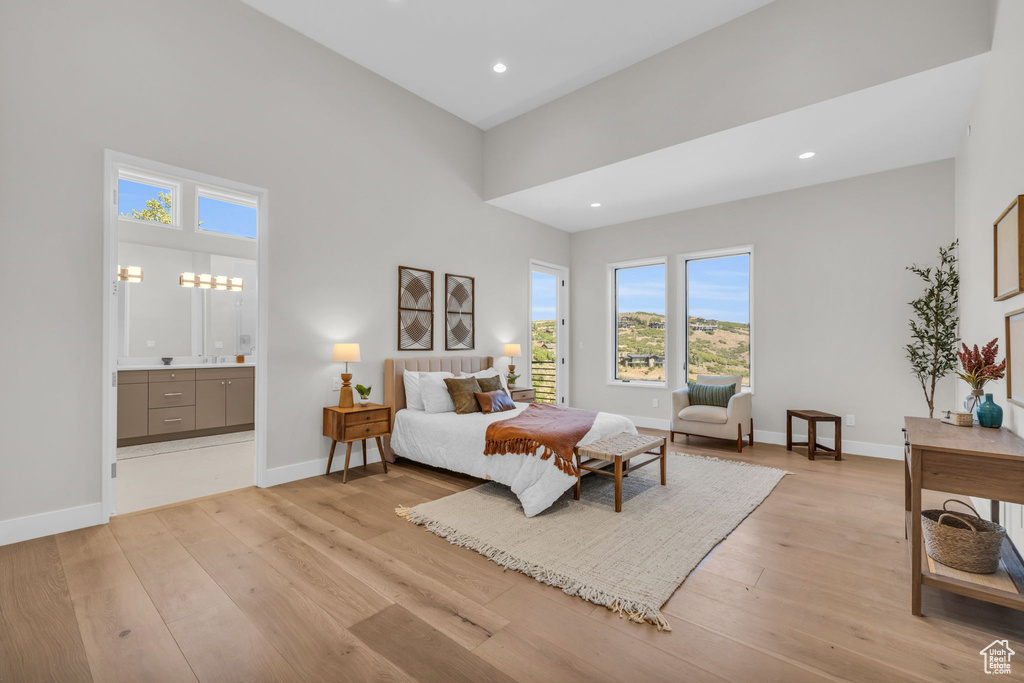 Bedroom with light hardwood / wood-style floors, ensuite bath, and a high ceiling