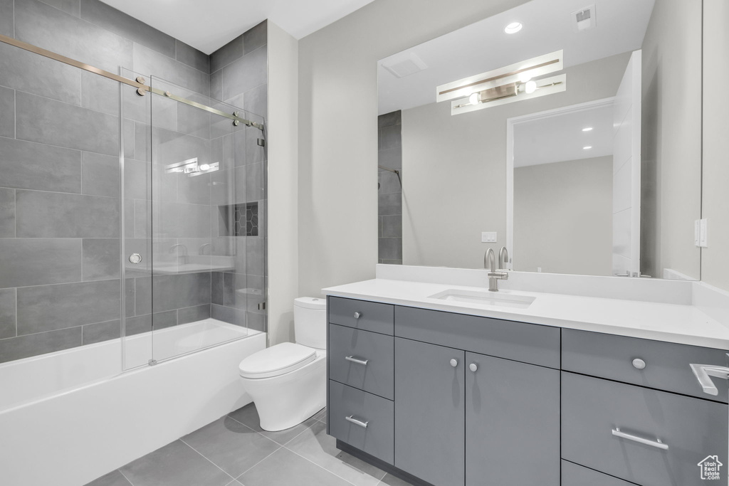 Full bathroom with shower / bath combination with glass door, vanity, tile patterned floors, and toilet