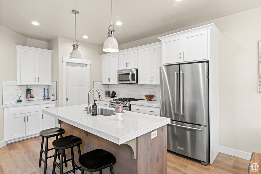 Kitchen featuring backsplash, appliances with stainless steel finishes, light hardwood / wood-style flooring, and a kitchen island with sink